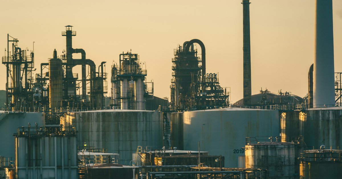 Oil refinery with storage tanks and metal pipes under a warm golden sky