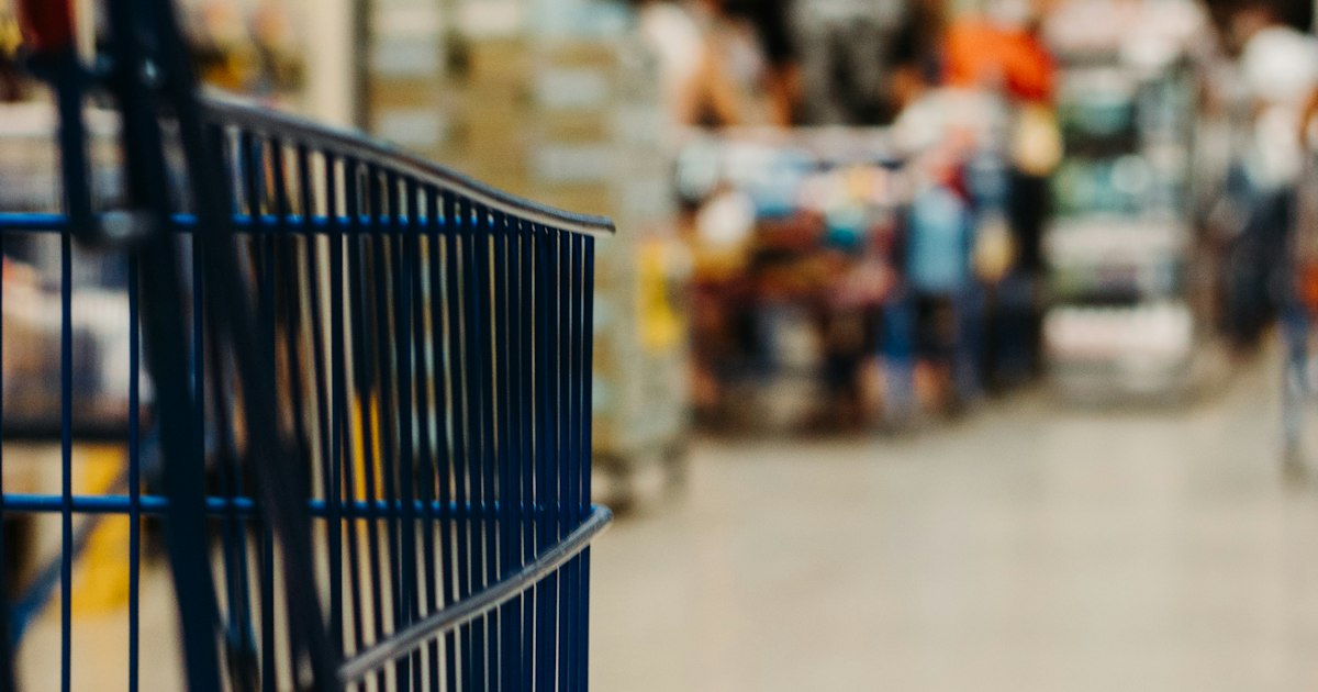 Empty blue metal shopping cart in a blurred grocery store aisle